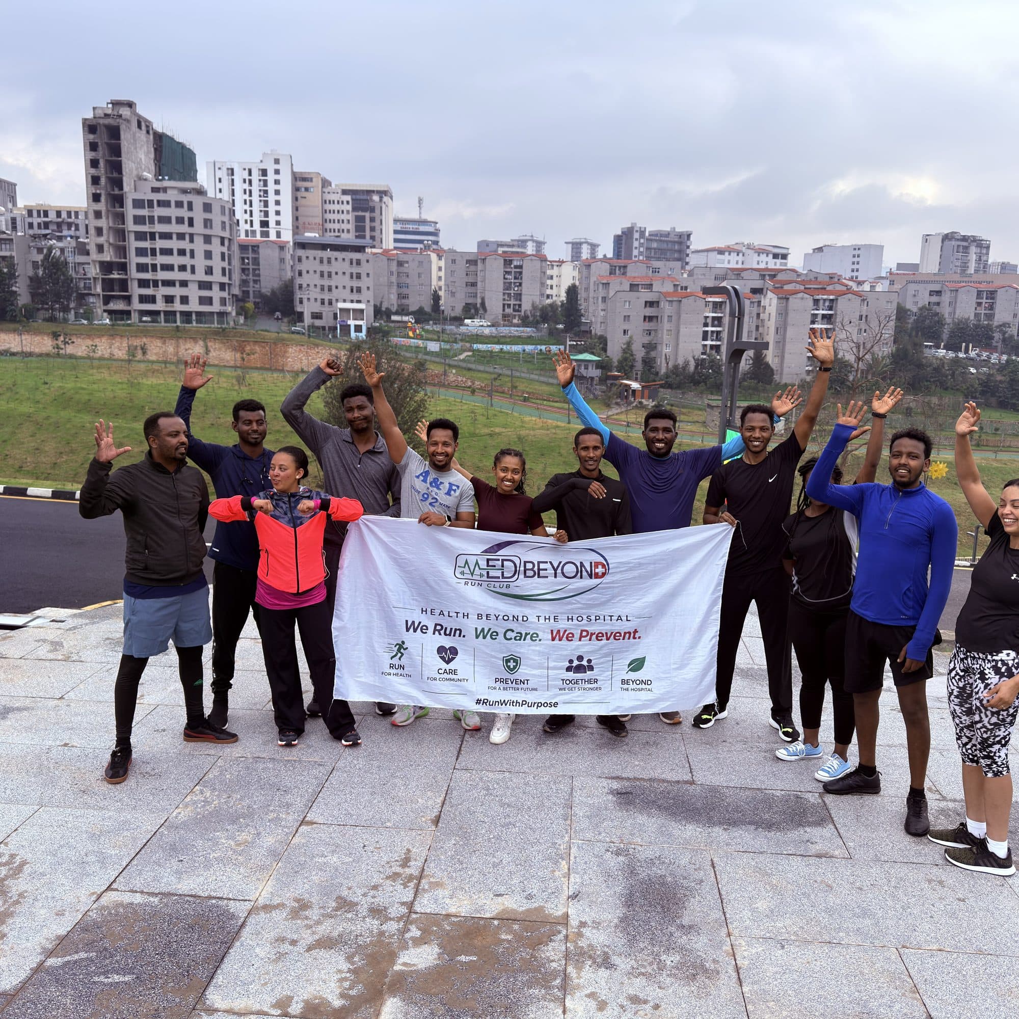 MedBeyond Run Club members celebrating with raised arms behind the club banner, Addis Ababa skyline in the background